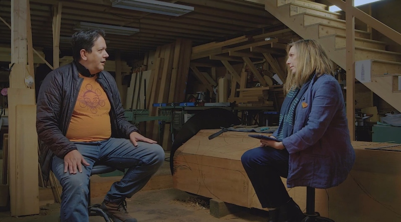 Man and woman sitting on stools in a carpenter workshop, surrounded by wood and tools